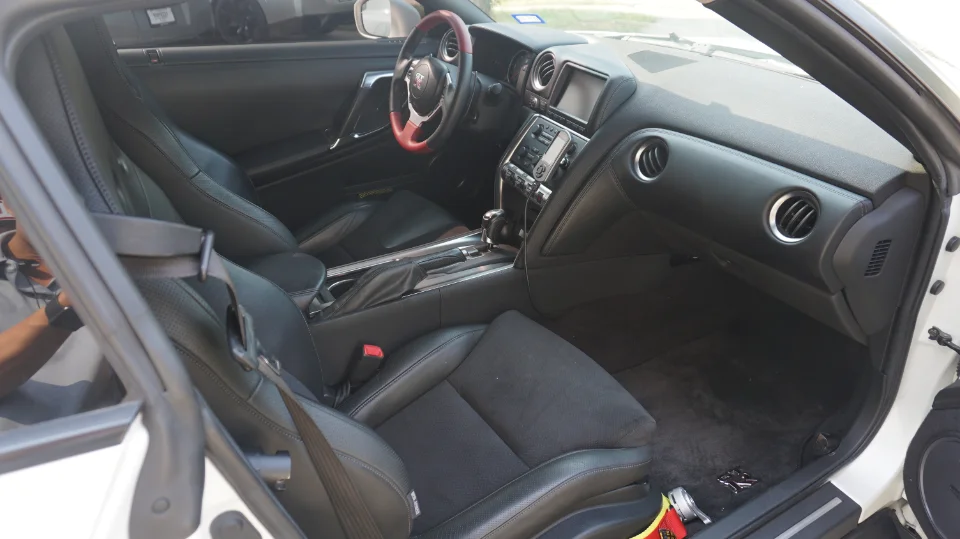 Interior view of a Nissan GT-R with black leather seats, red and black steering wheel, and detailed dashboard.