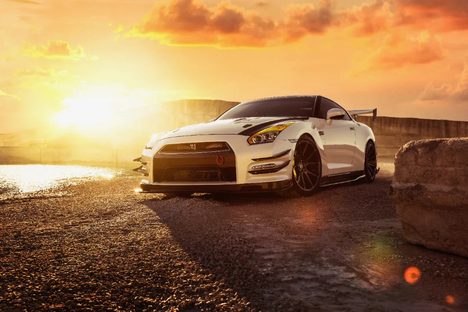 A white Nissan GT-R with an aggressive aero kit and aftermarket wheels parked on a gravel road at sunset.