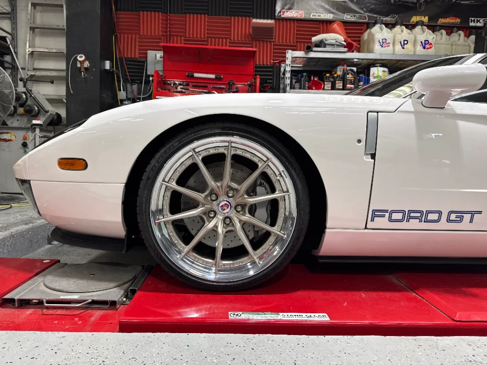 White Ford GT on a dyno at a performance tuning shop, showcasing custom wheels and brakes.