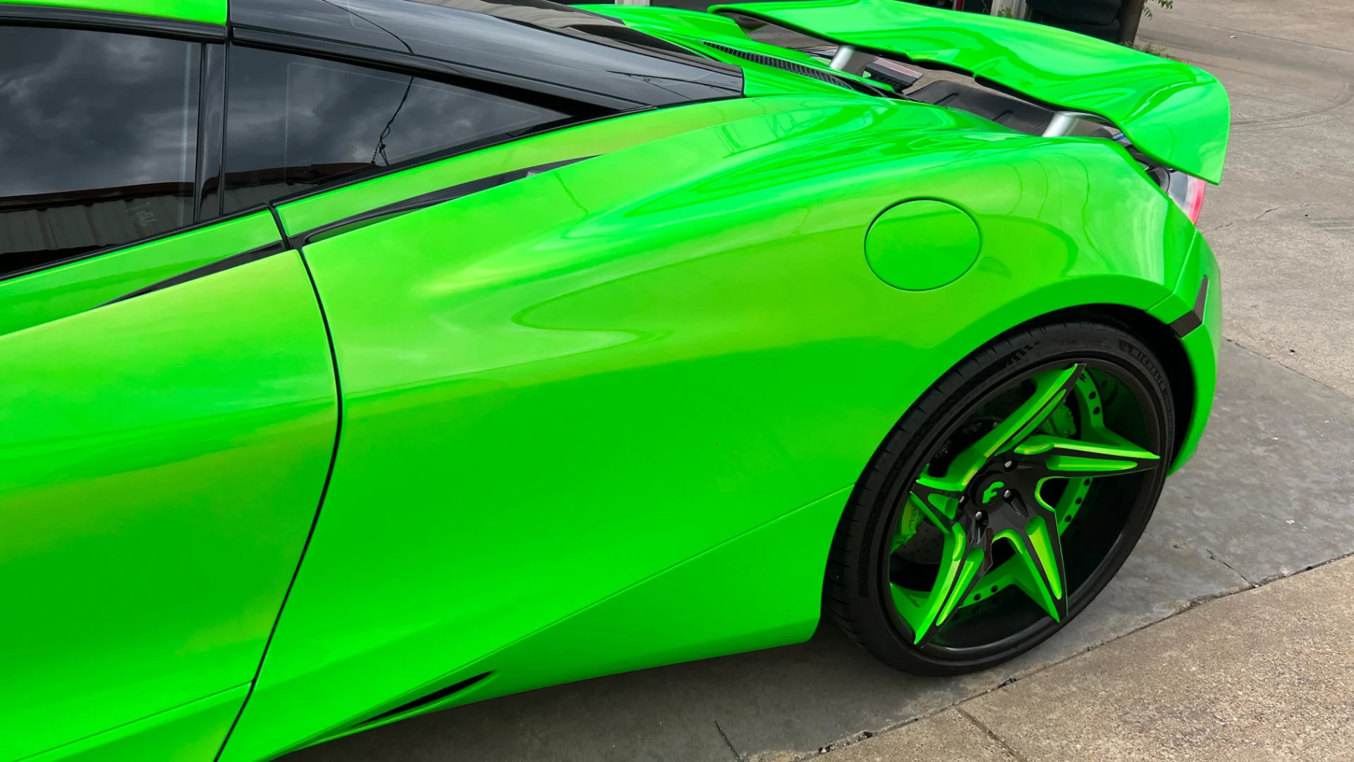 Close-up of a bright green McLaren supercar, showcasing its custom green and black multi-spoke wheels.