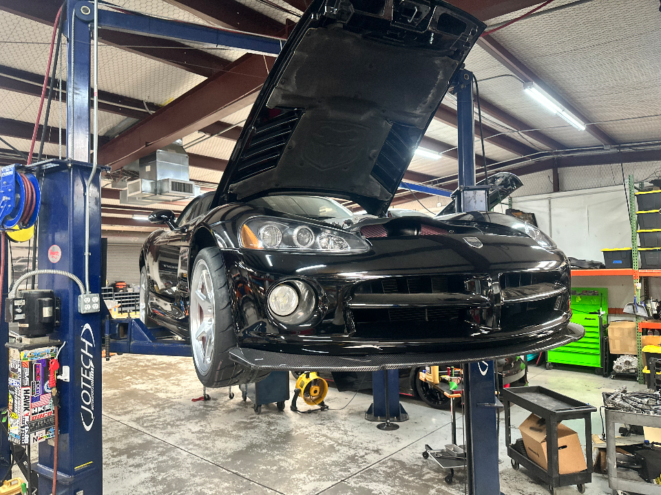 A black Dodge Viper on a car lift in a performance tuning shop with its hood open, showcasing the engine bay and a carbon fiber front splitter.