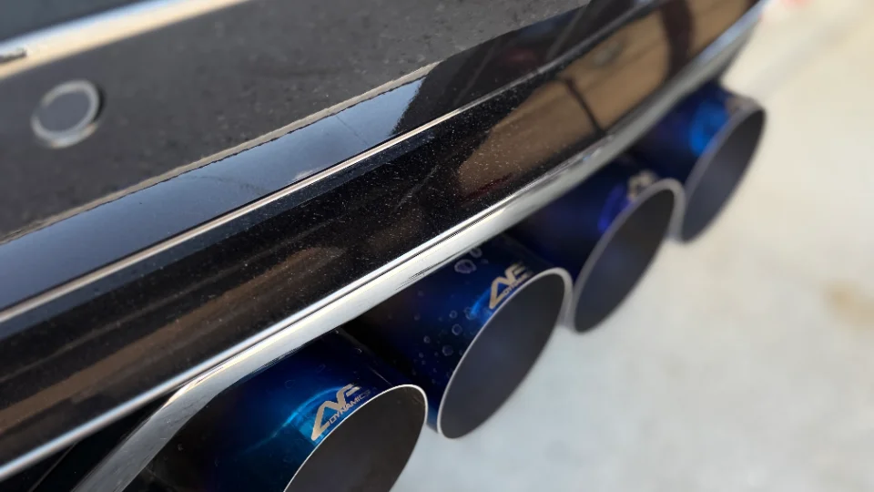 Close-up of blue titanium quad exhaust tips on a performance car, featuring AE Dynamics branding.