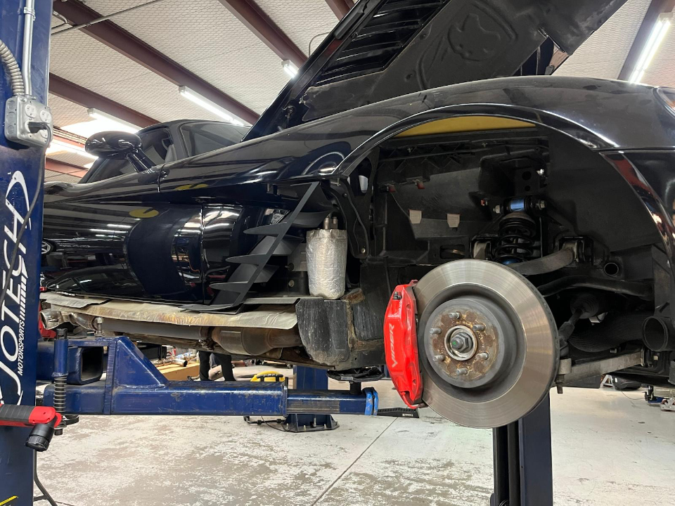 A black Dodge Viper on a lift in a performance shop, with the front wheel removed to show the red brake caliper and suspension.