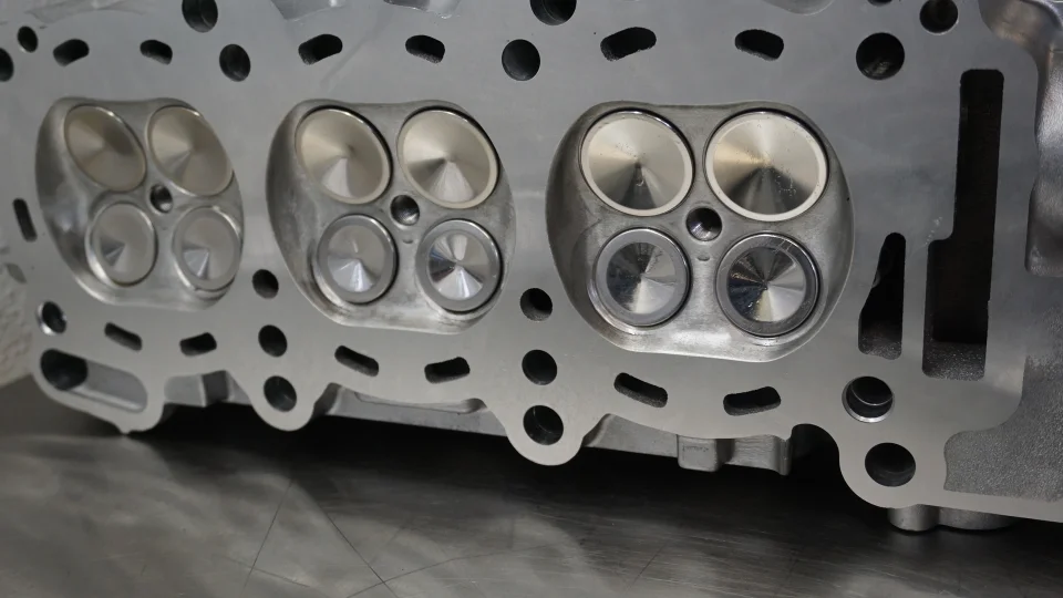 A close-up view of a precision-machined aluminum engine cylinder head with intake and exhaust valves.