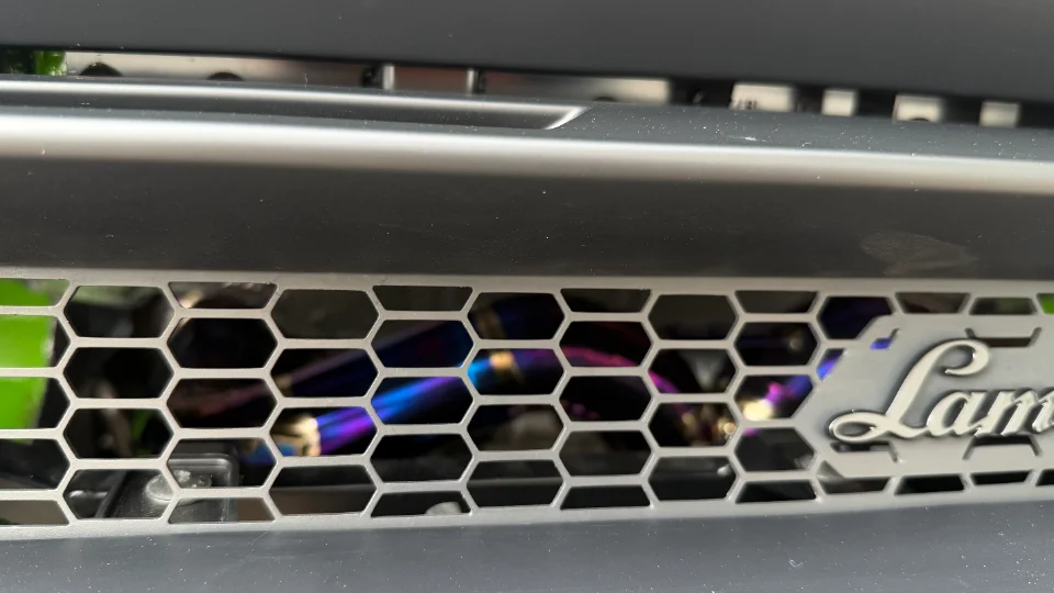 Close-up detail of a Lamborghini's front grille revealing colorful aftermarket titanium exhaust piping.