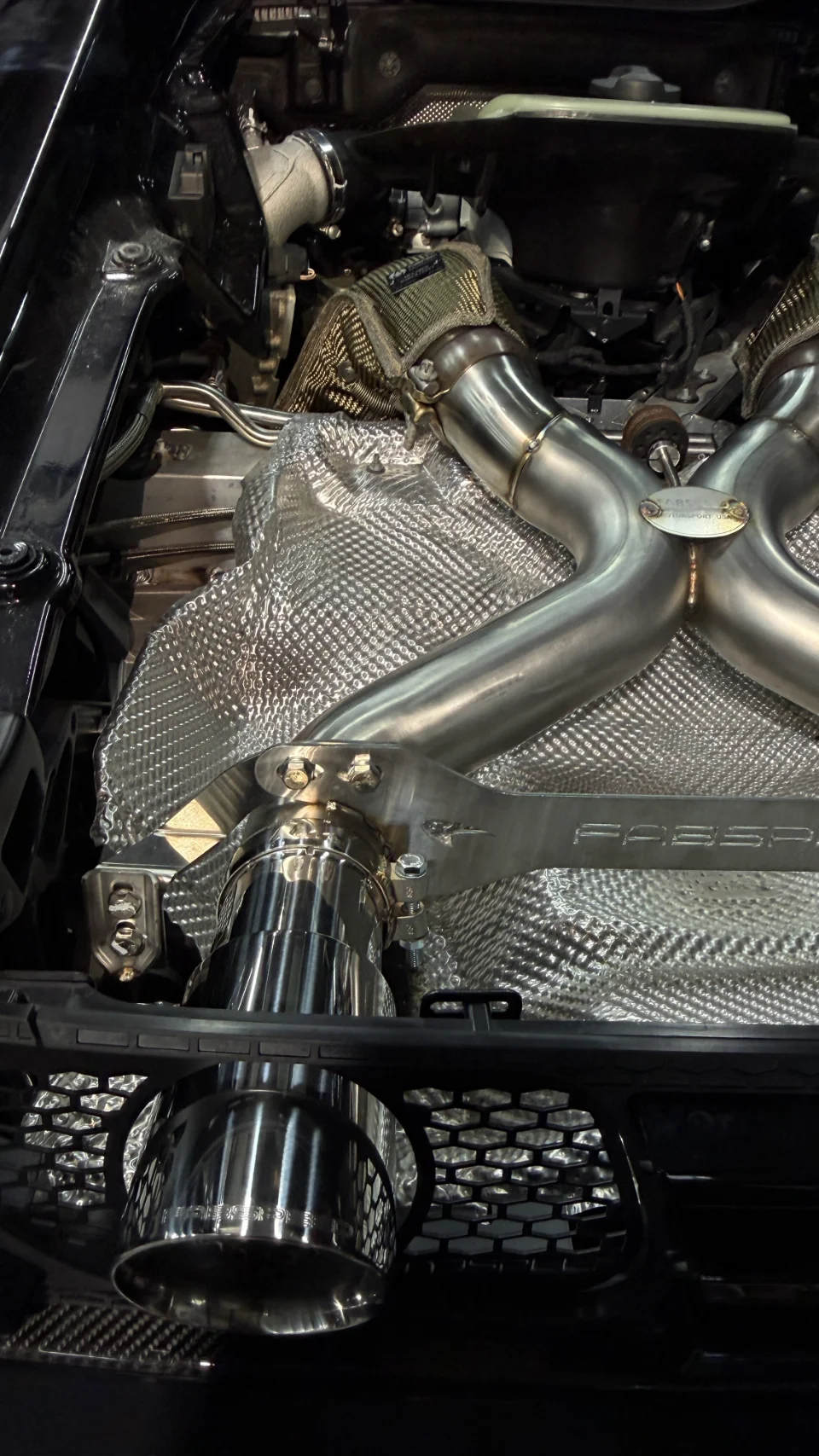 A close-up view of a Fabspeed aftermarket exhaust system with heat shielding installed in a high-performance car's engine bay.