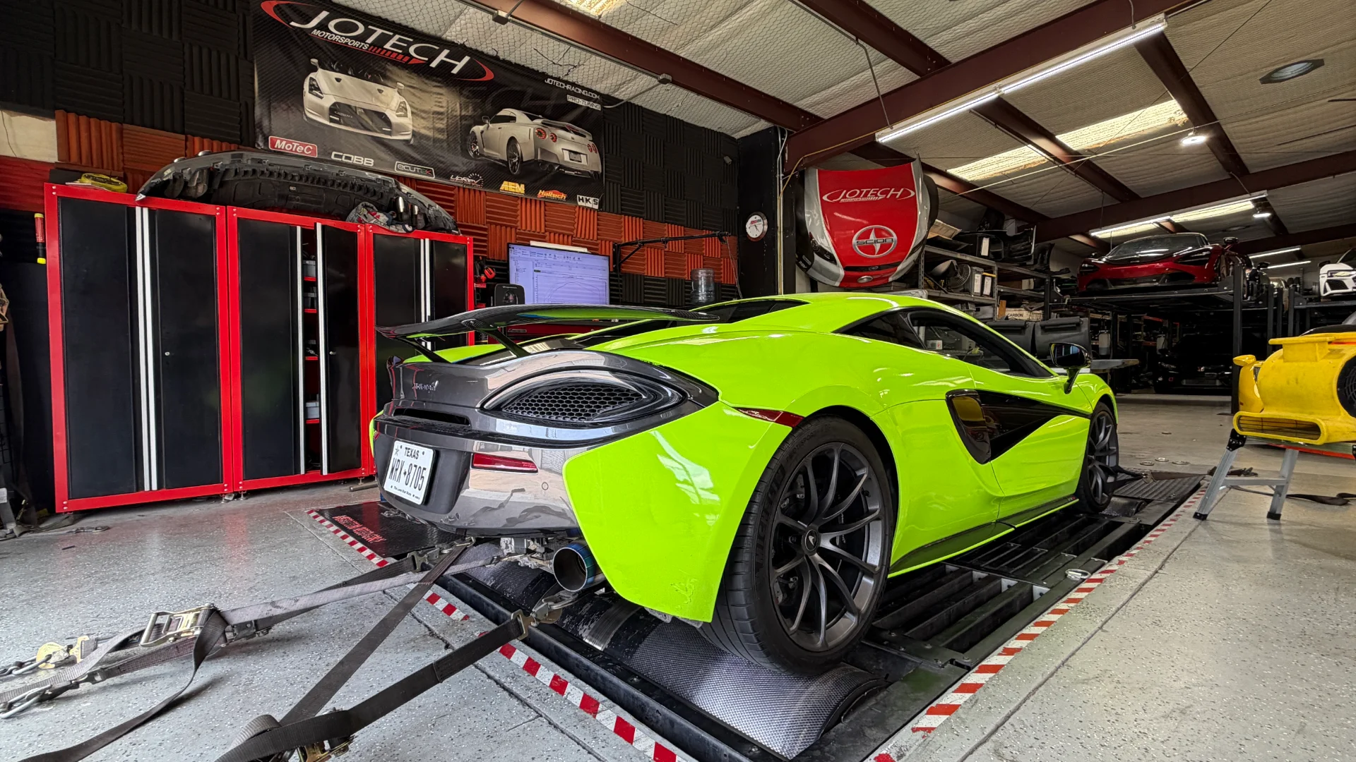 A neon green McLaren supercar strapped to a dynamometer at Jotech Motorsports for performance tuning.