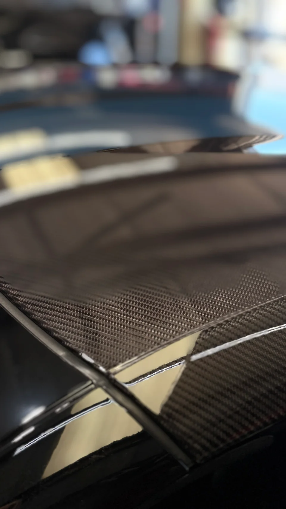 A close-up detail shot of a carbon fiber car part, showcasing its intricate weave and glossy finish.