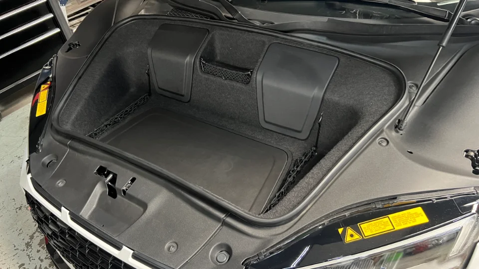 Open front trunk of a black Audi R8, showing the carpeted storage area and netting in a shop setting.
