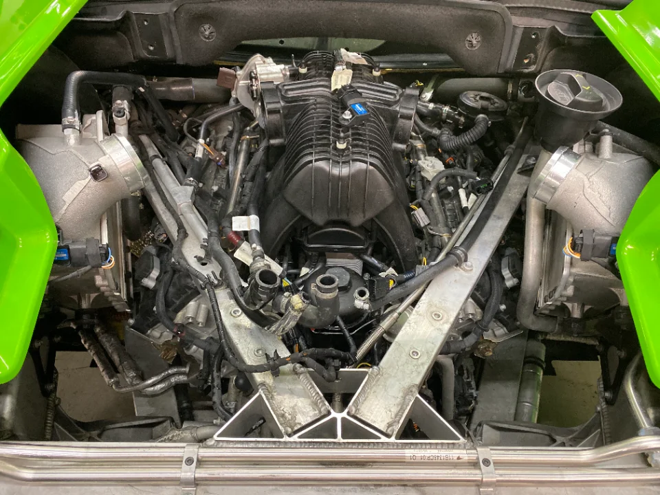 A detailed view of a Lamborghini engine bay featuring a prominent supercharger and performance induction components.