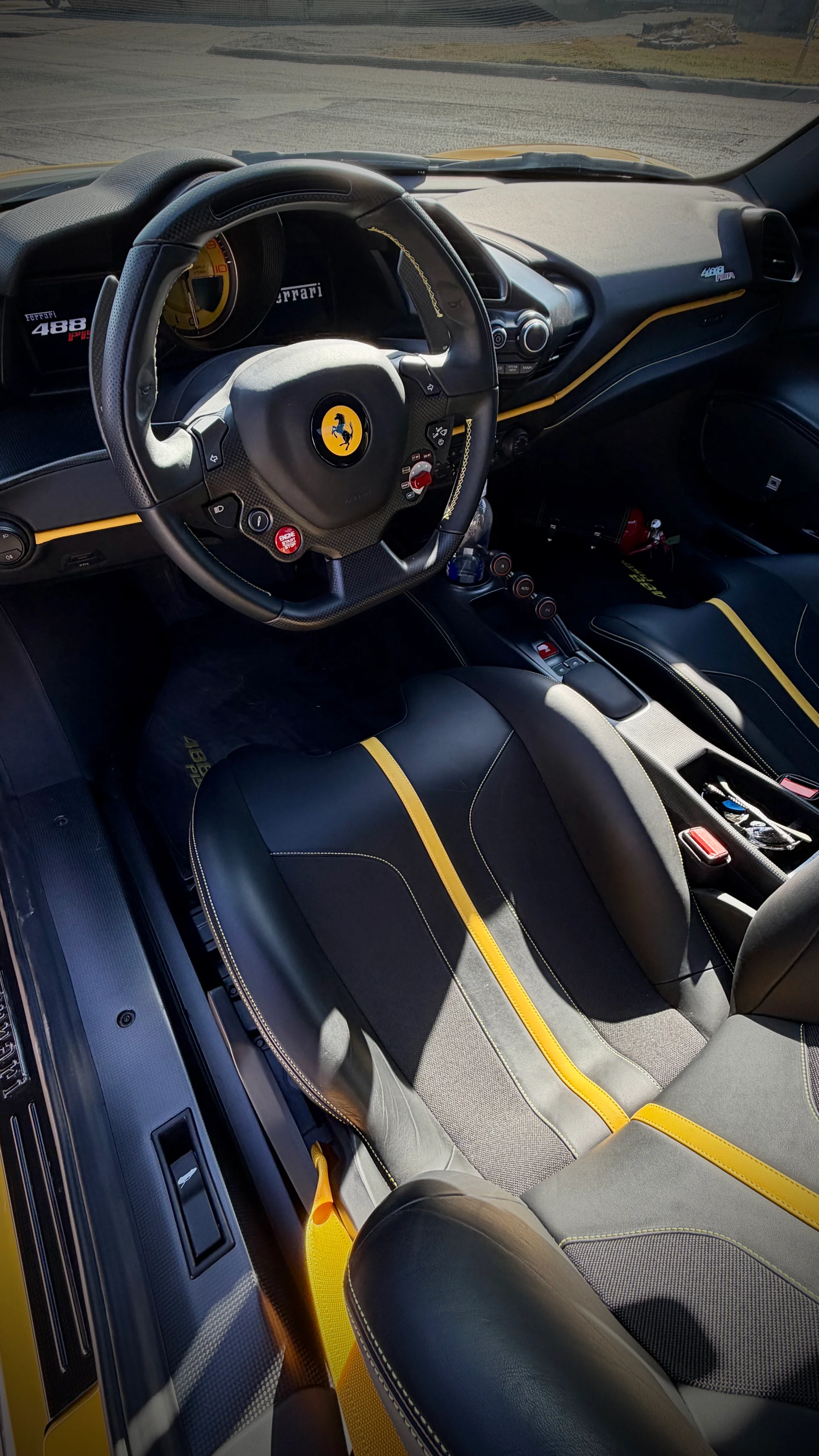 Interior view of a yellow Ferrari 488 Pista, showcasing the black and yellow leather seats, carbon fiber steering wheel, and dashboard.