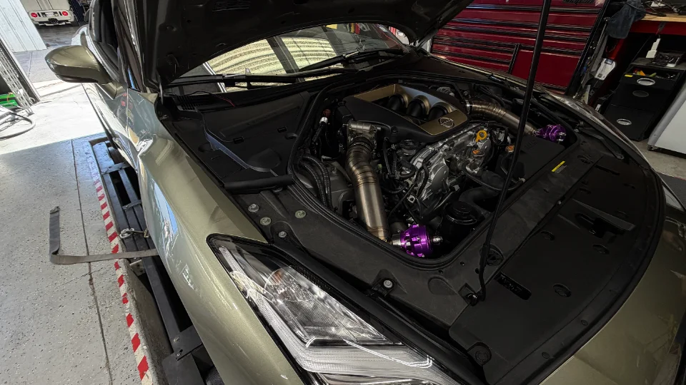 A Nissan GT-R with its hood open on a dyno, showcasing a custom engine bay with aftermarket induction and turbo components.