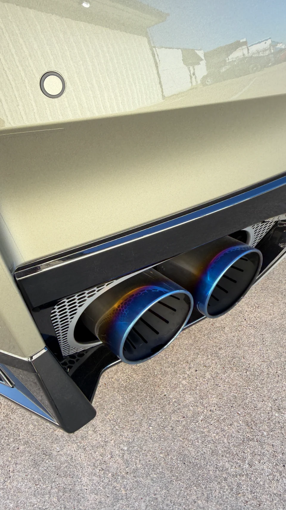Close-up of a car's rear bumper featuring iridescent titanium exhaust tips.
