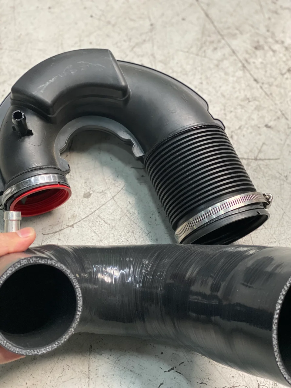 Aftermarket intake pipe and silicone hose for a performance car's induction system, laid on a shop floor.