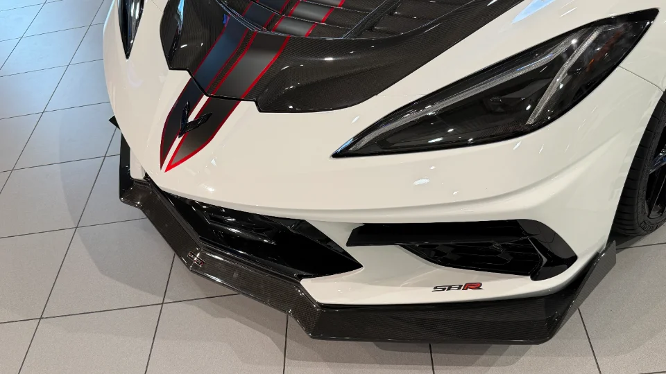 Close-up of a white C8 Corvette front end with carbon fiber hood, splitter, and red racing stripes.