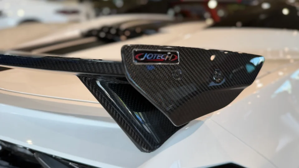 A close-up of a Jotech carbon fiber wing on a white performance car.