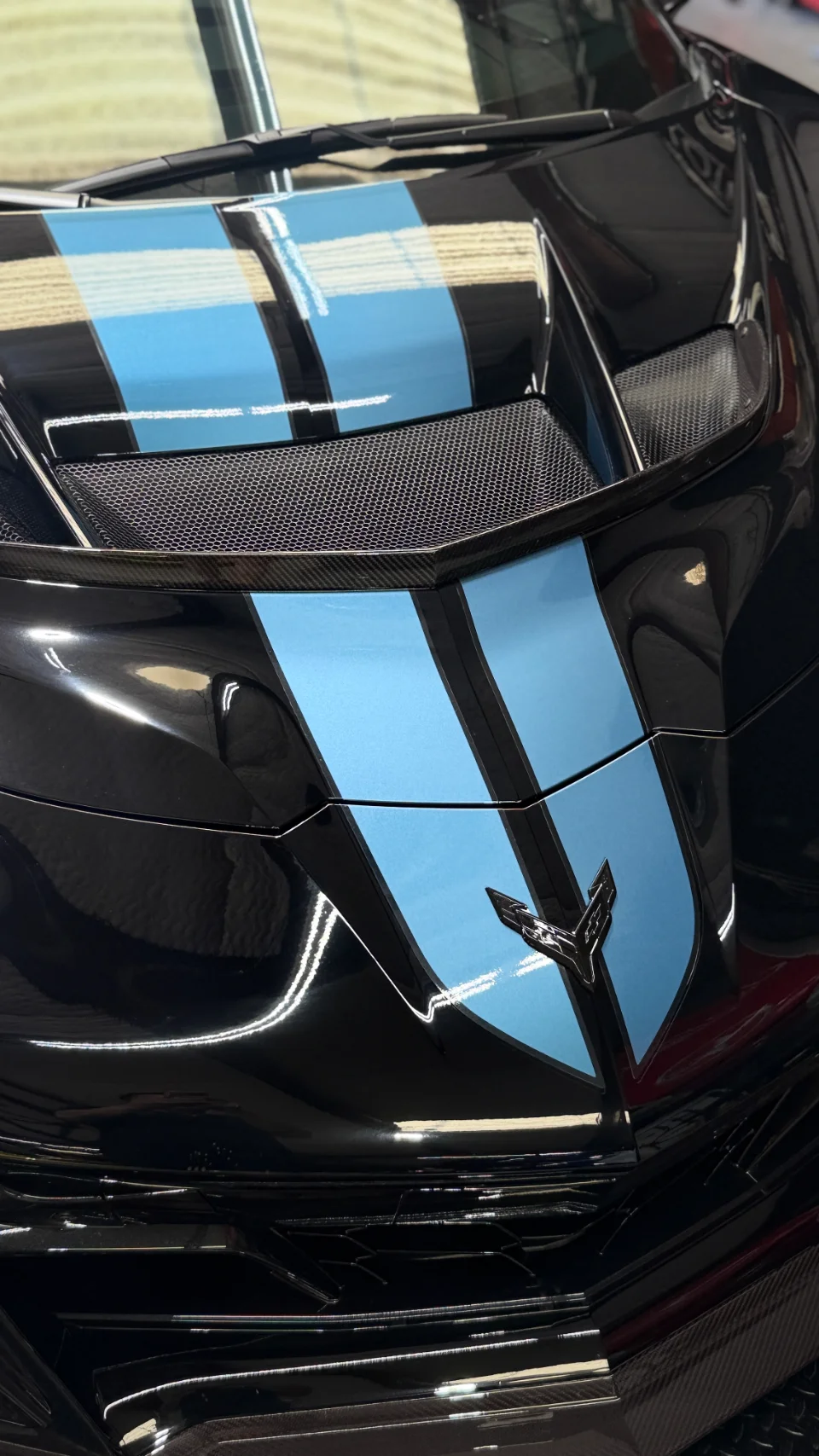 Close-up of a black C8 Corvette front hood with blue racing stripes and carbon fiber vents.