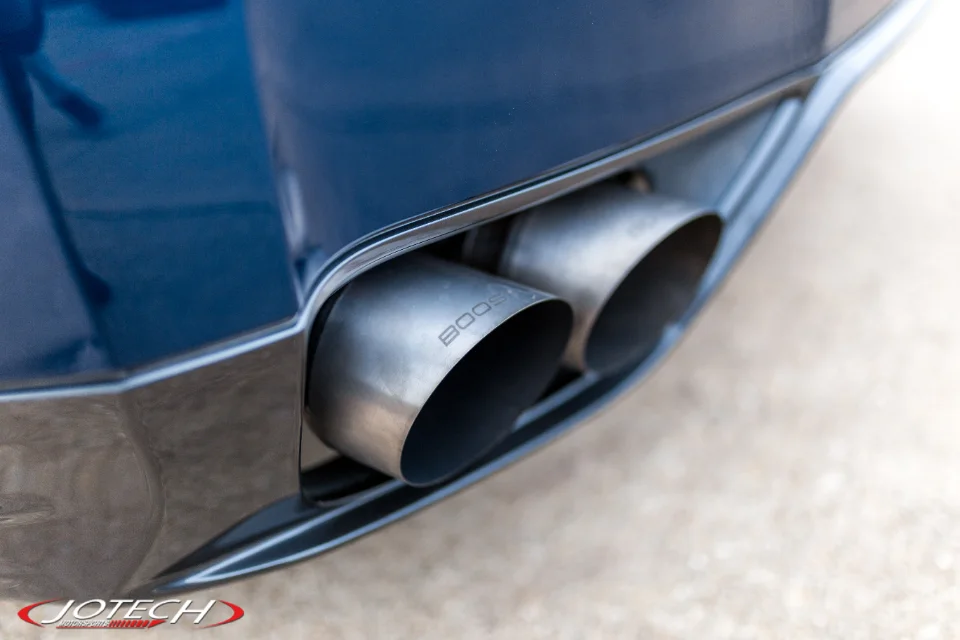 Close-up of custom exhaust tips with 'BOOST' engraving on a blue performance car, likely a Jotech build.