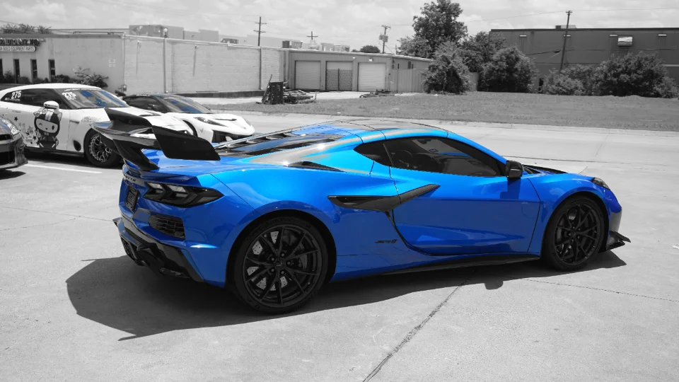 Blue Chevrolet Corvette C8 Z06 with a large rear wing and carbon fiber aero parked at Jotech Motorsports with other cars.