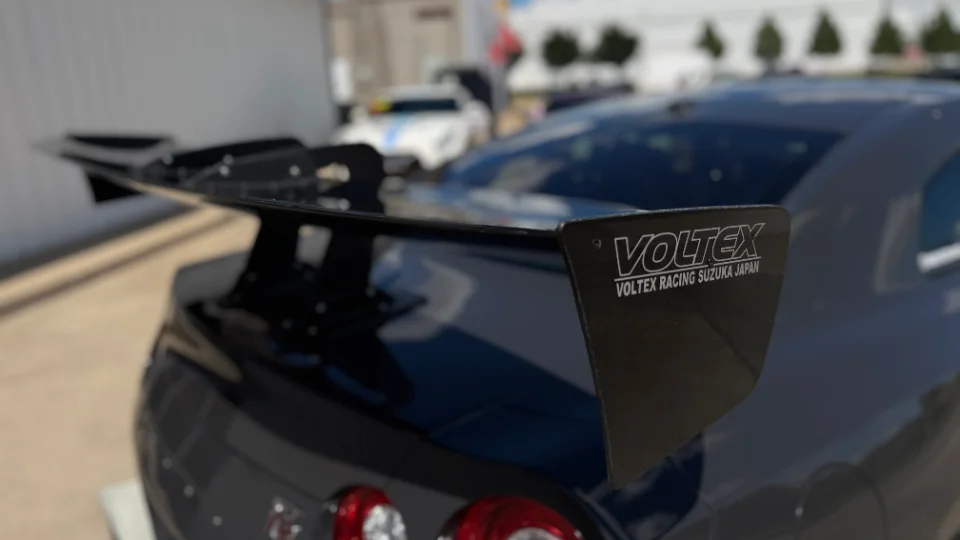 Close-up of a black Voltex carbon fiber rear wing on a Nissan GT-R, showcasing the aerodynamic detail.
