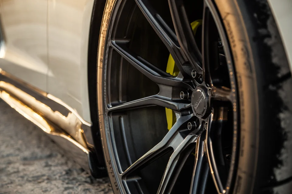 Close-up of a white car's custom dark multi-spoke wheel with yellow brake calipers and a performance tire.