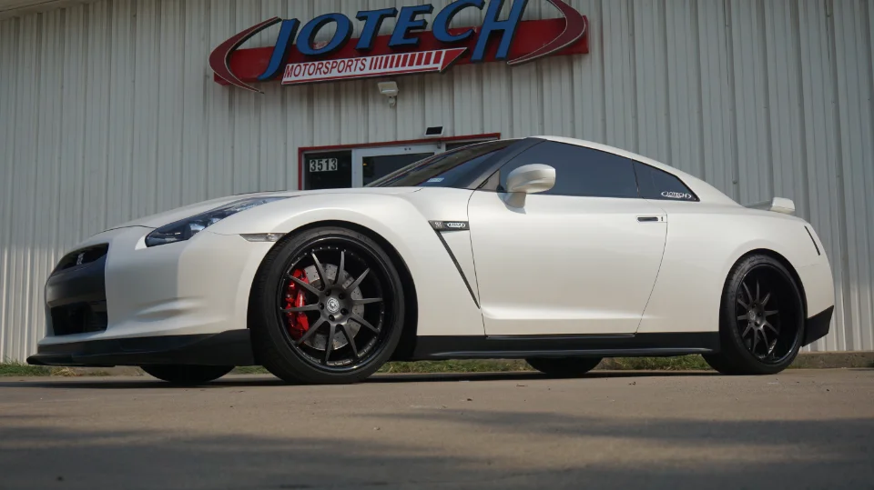 White Nissan GT-R with aftermarket wheels and red calipers parked in front of Jotech Motorsports shop.