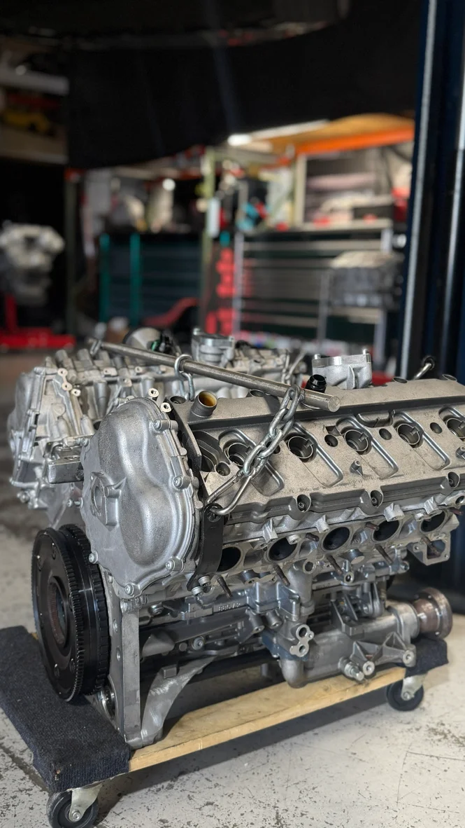 A V8 engine block with cylinder heads on a dolly in a performance tuning shop, ready for assembly or installation.