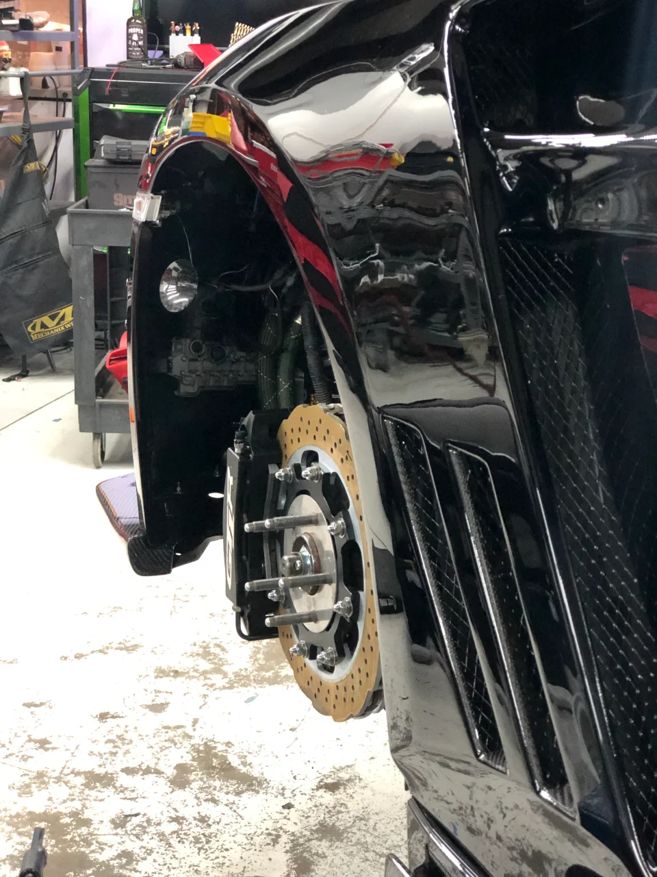 Close-up of a black performance car in a shop with the wheel removed, showcasing the drilled brake rotor and caliper.