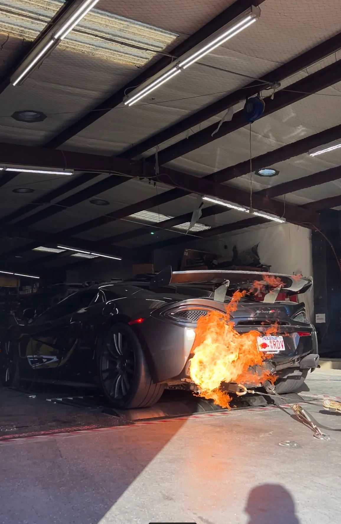 A McLaren supercar on a dyno with large flames shooting from its exhaust during a performance test in a tuning shop.