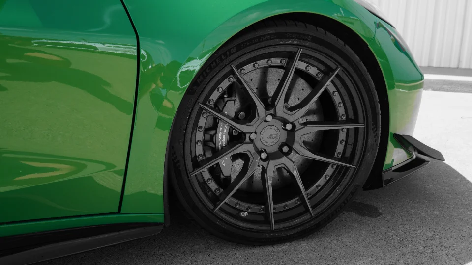 A close-up of a vibrant green Corvette's custom black multi-spoke wheel, Michelin tire, and performance brake caliper.