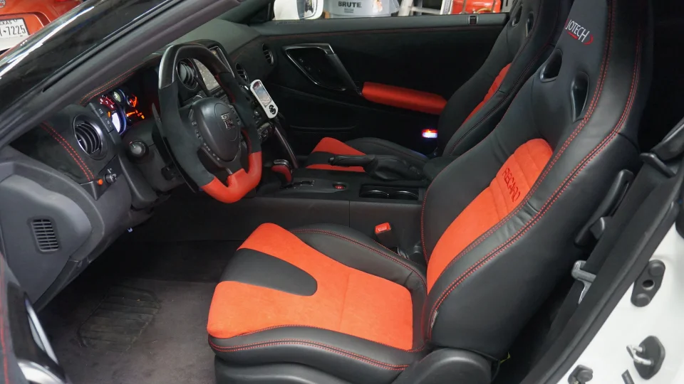 Interior view of a Nissan GT-R featuring black and red Recaro seats, custom steering wheel, and red stitching.