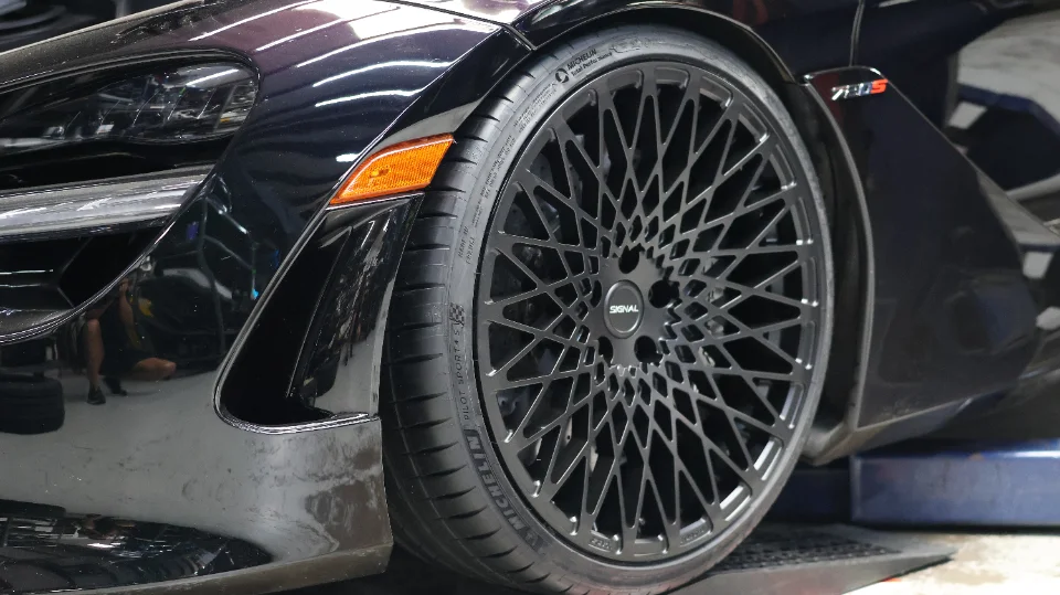 Close-up of a black McLaren 720S front wheel with black Signal wheels and Michelin Pilot Sport 4S tires in a shop.