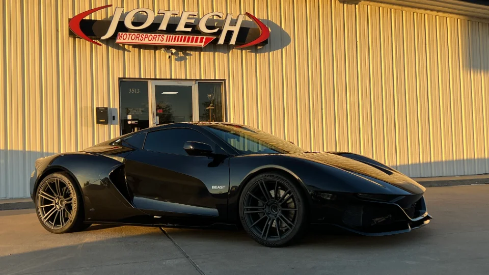 Black Rezvani Beast supercar parked outside Jotech Motorsports performance tuning shop with its logo visible.