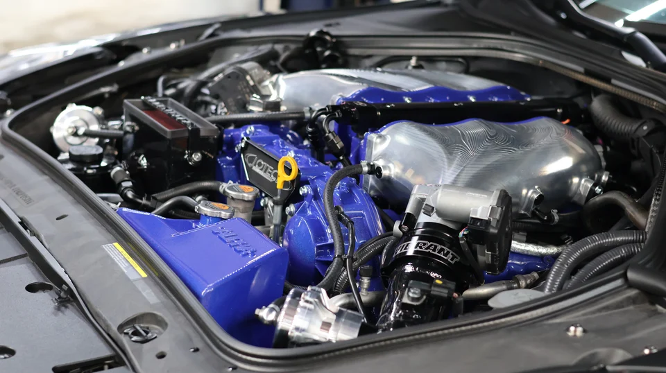 A detailed view of a high-performance Nissan GT-R engine bay featuring custom blue and polished silver aftermarket components.