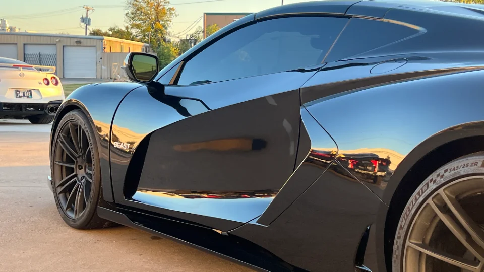 A sleek black C8 Corvette with custom widebody and wheels parked outdoors, with a white Nissan GT-R in the background.