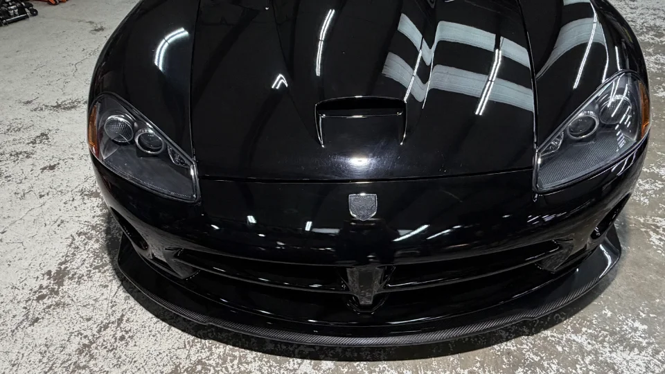 Front view of a shiny black Dodge Viper with a carbon fiber front splitter and hood scoop.