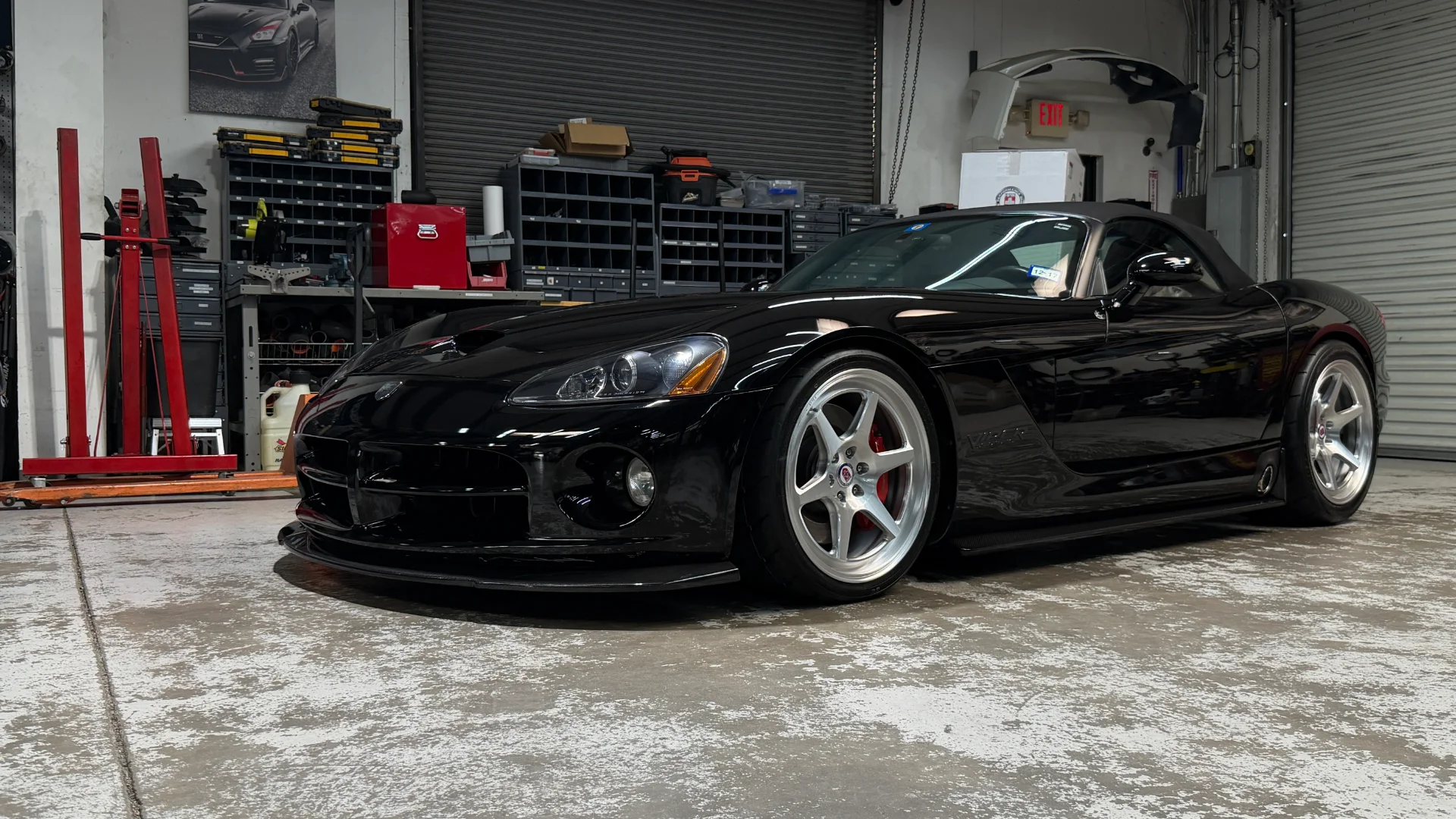 A sleek black Dodge Viper with custom silver wheels and red brake calipers is perfectly parked inside a performance shop.