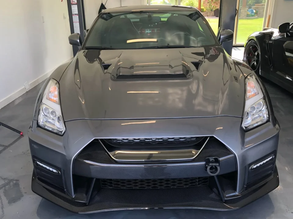 Front view of a grey Nissan GT-R with a carbon fiber front bumper, splitter, and hood scoop in a garage.