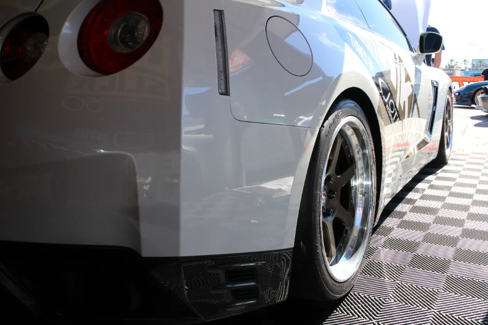 Rear view of a white Nissan GT-R with aftermarket wheels and a carbon fiber rear diffuser, parked on a checkered floor.