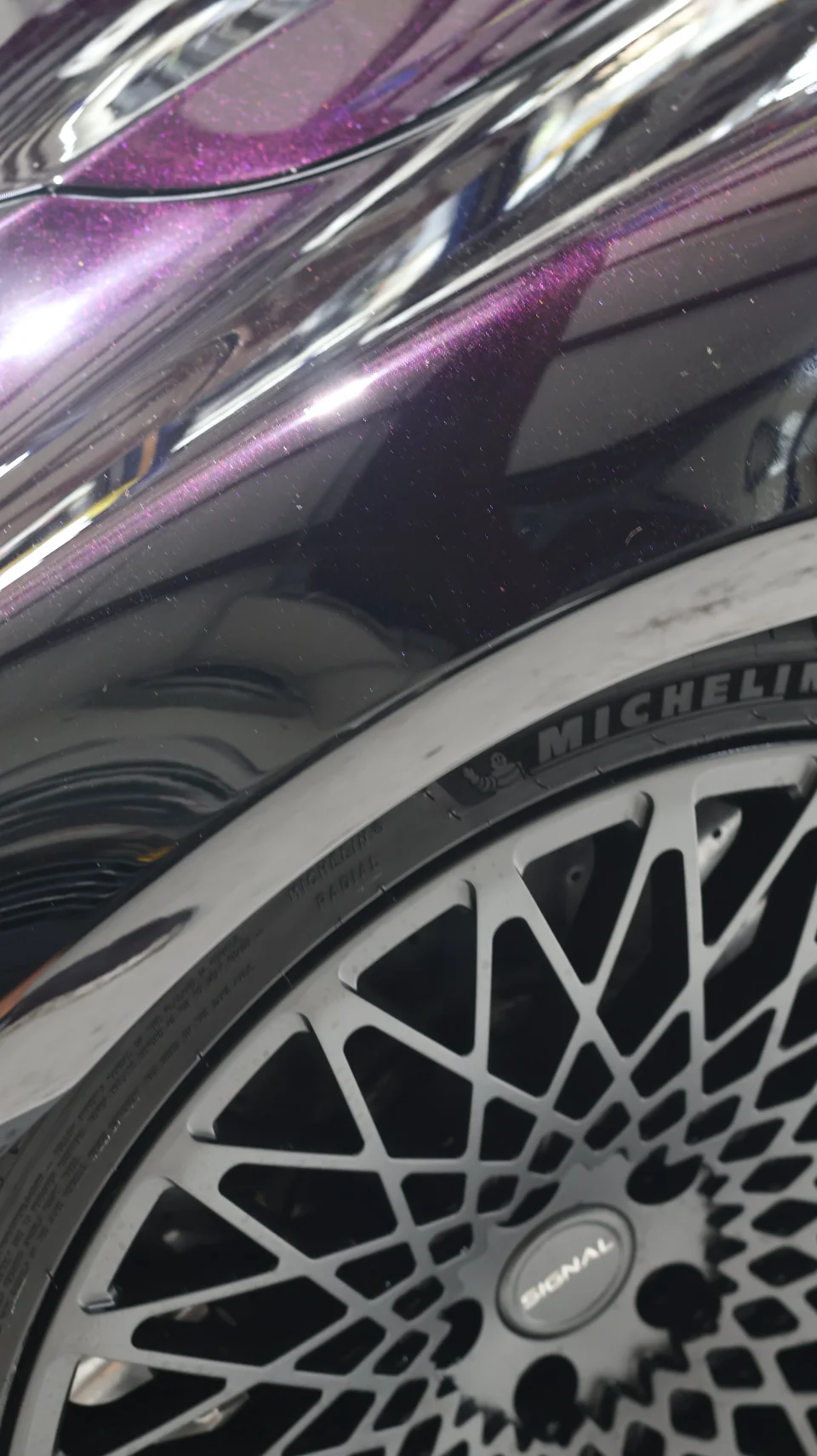 A close-up of a car's purple metallic fender and a black multi-spoke Signal wheel with Michelin tires.