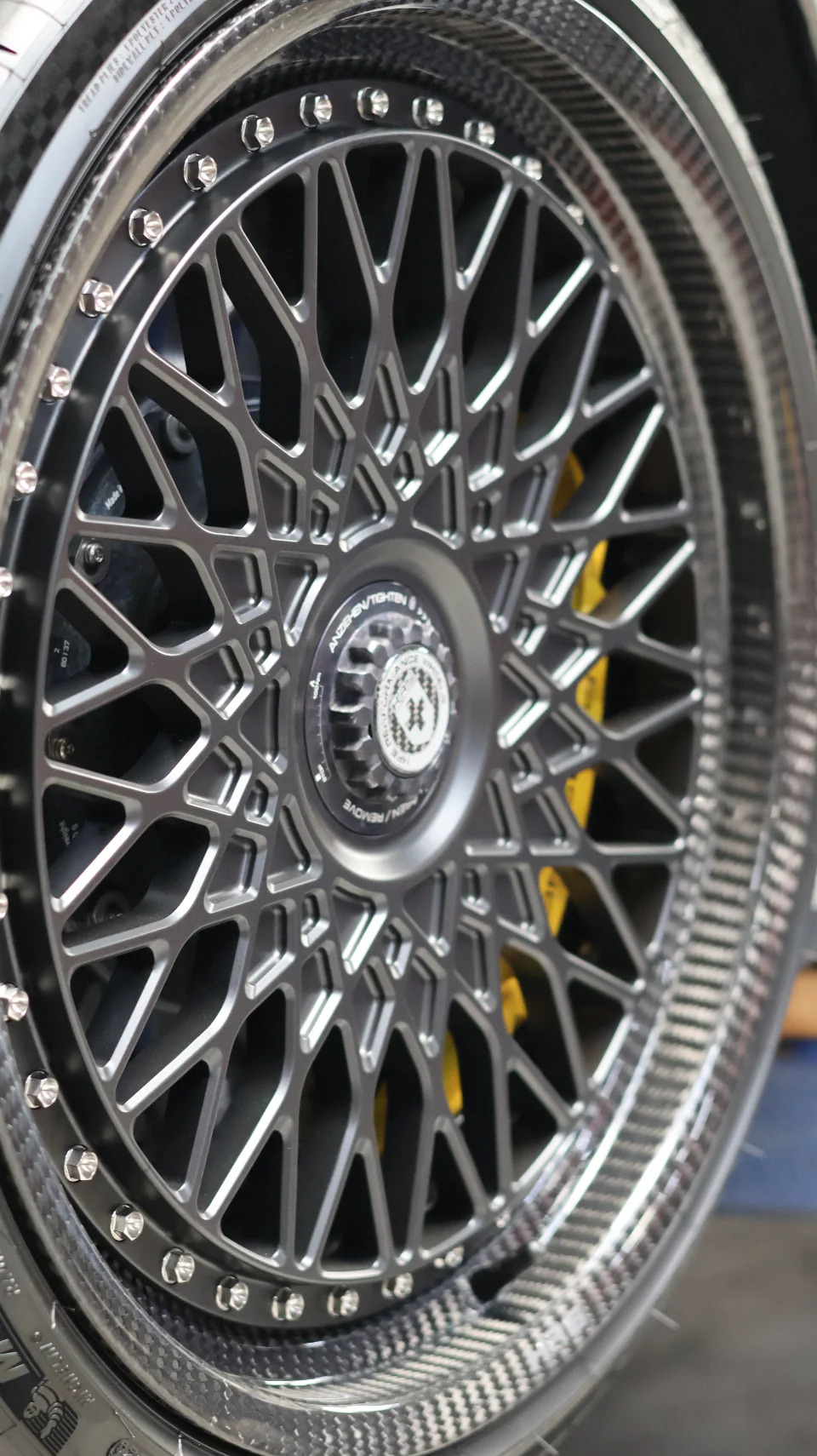 Close-up of a multi-spoke wheel with a carbon fiber barrel and a yellow brake caliper visible behind the spokes.