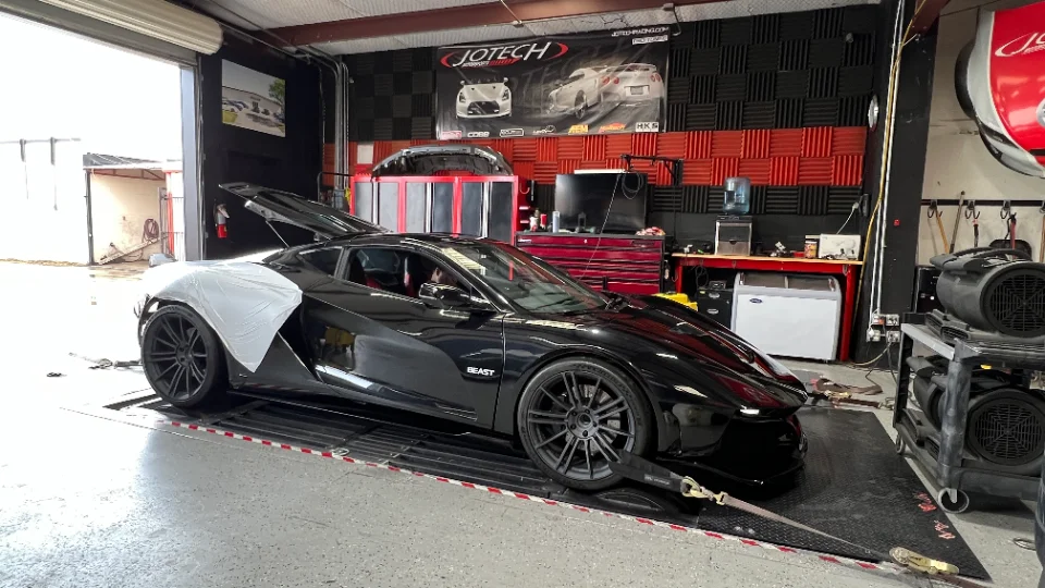 Black McLaren supercar strapped to a dynamometer for performance tuning at a Jotech Motorsports facility.