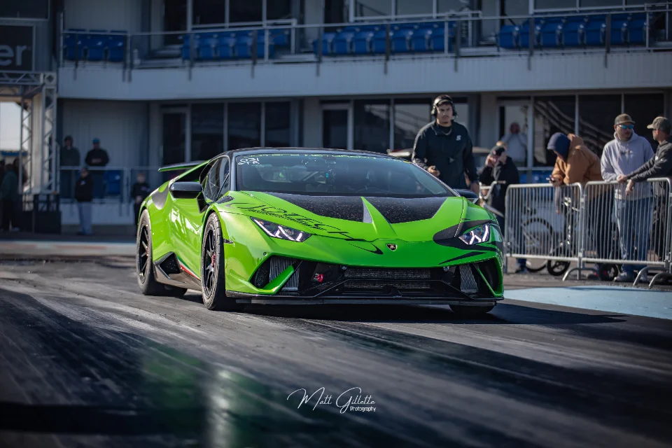 Bright green Lamborghini Huracan on a drag strip, with tire marks on the asphalt and spectators in the background.
