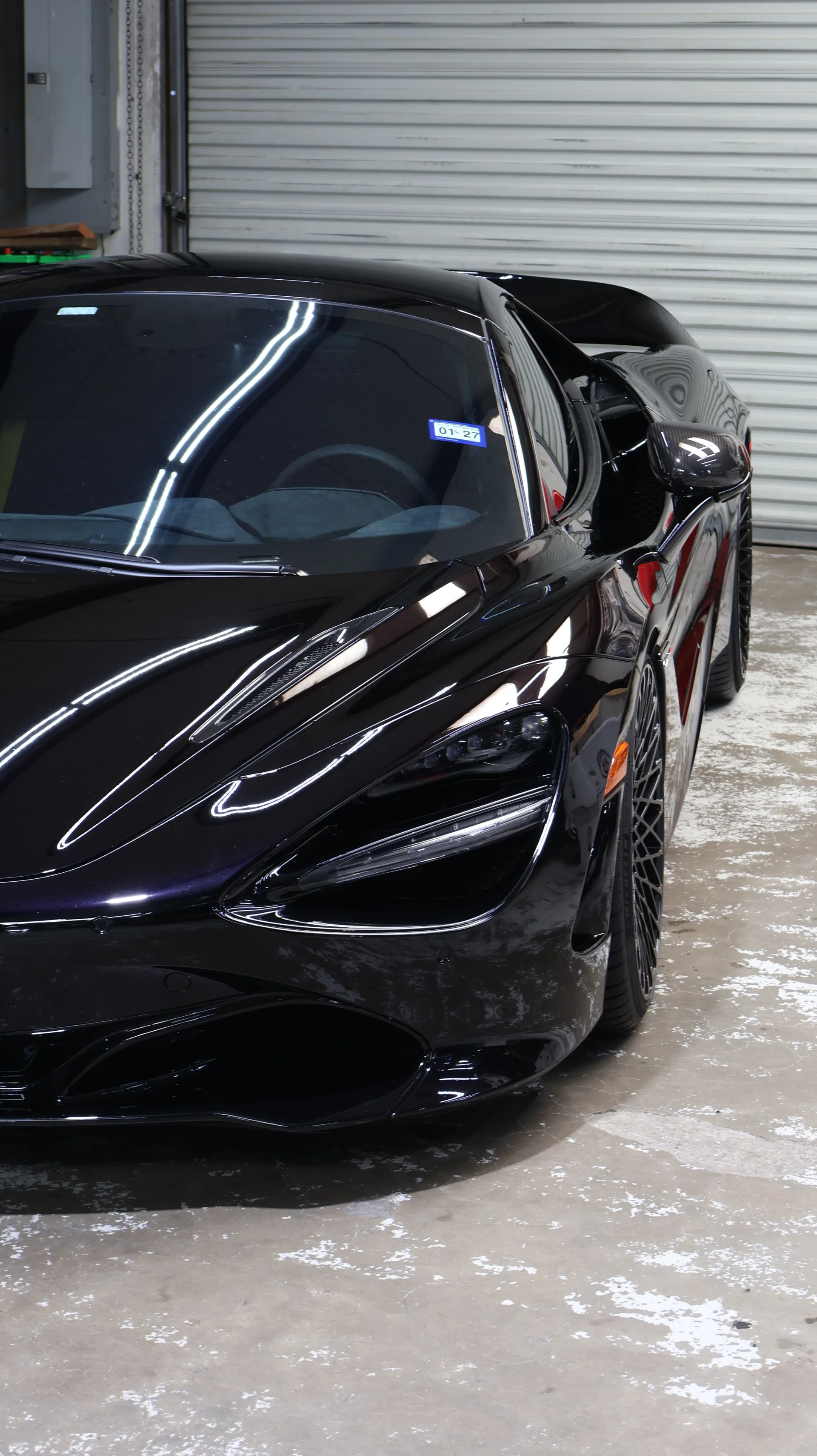A sleek black McLaren 720S supercar parked in a garage, showcasing its glossy finish and aggressive front design.