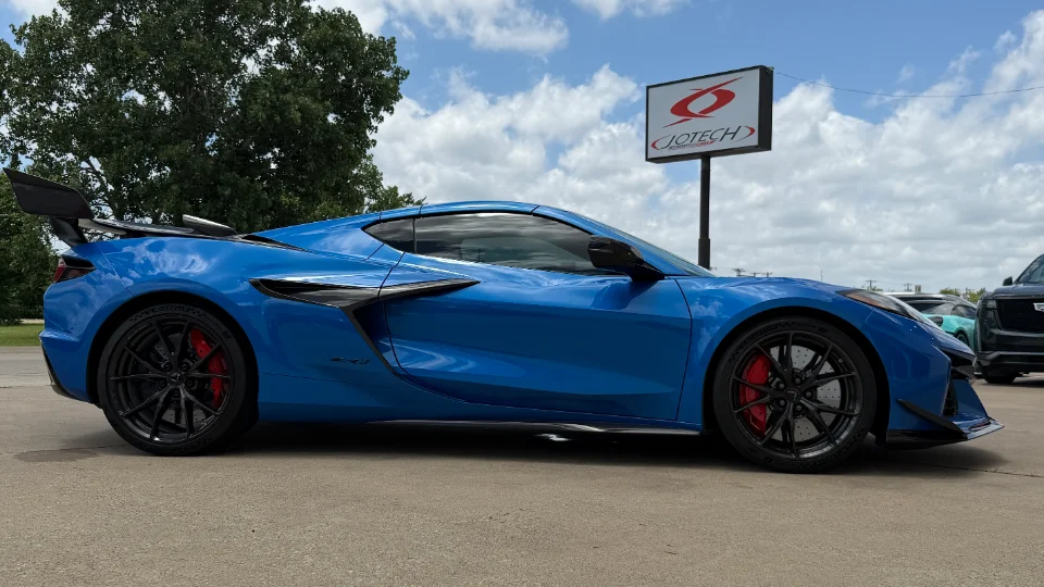 A blue Chevrolet Corvette C8 Z06 with a carbon fiber wing and black wheels parked outside Jotech Motorsports.