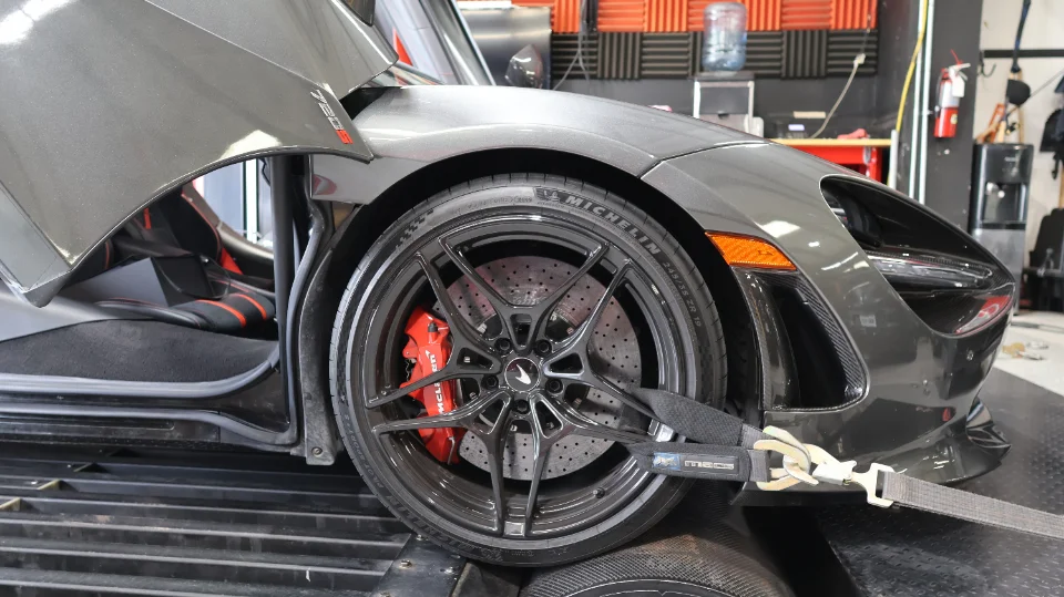 A grey McLaren 720S strapped to a dyno, showing the front wheel with red brake calipers and Michelin tires.