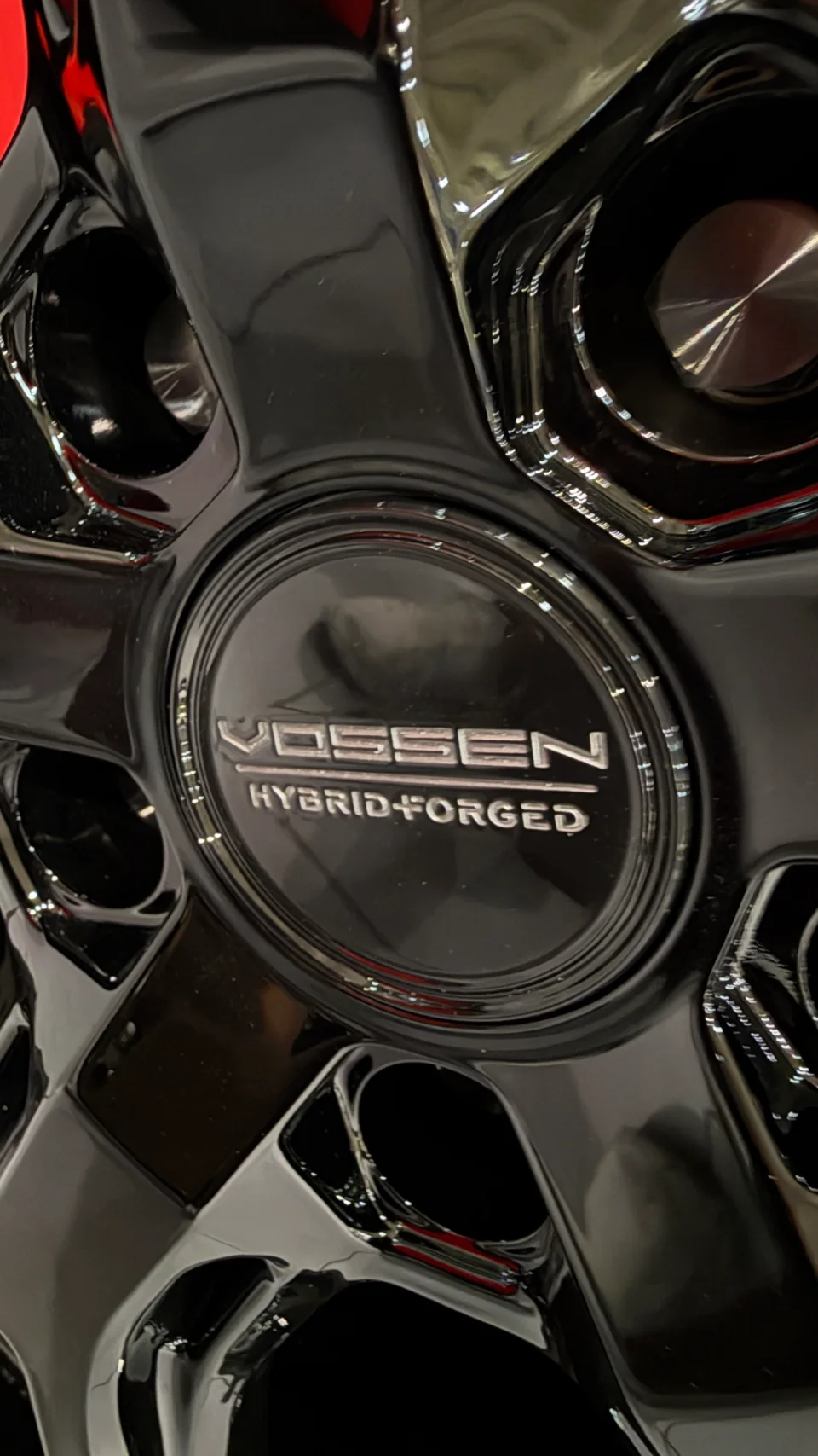 Close-up of a black Vossen Hybrid Forged wheel center cap, showcasing the brand and technology.