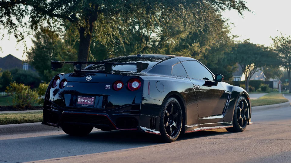 Rear view of a black Nissan GT-R with aftermarket wheels and a large rear wing parked on a residential street.