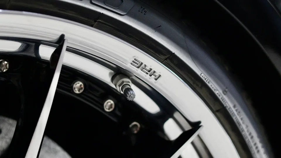 Close-up detail of a chrome HRE wheel and tire on a performance car, showcasing the wheel's design and brand.