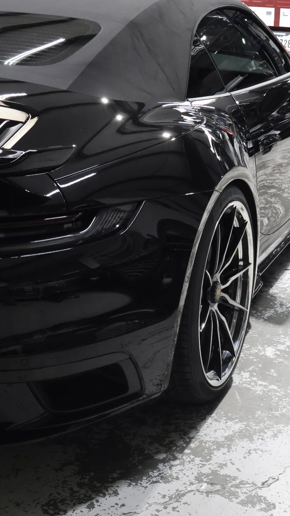 A black Porsche 911 convertible with custom wheels parked on a shop floor, showcasing its sleek rear design.